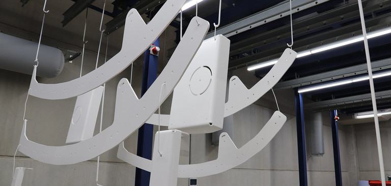 Grundierte Großteile hängen an Pulverbeschichtungsanlage