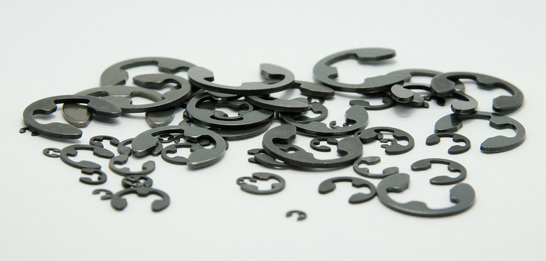 Viele halbringförmige schwarze Blechzuschnitte aus Federbandstahl liegen unordentlich auf- und nebeneinander